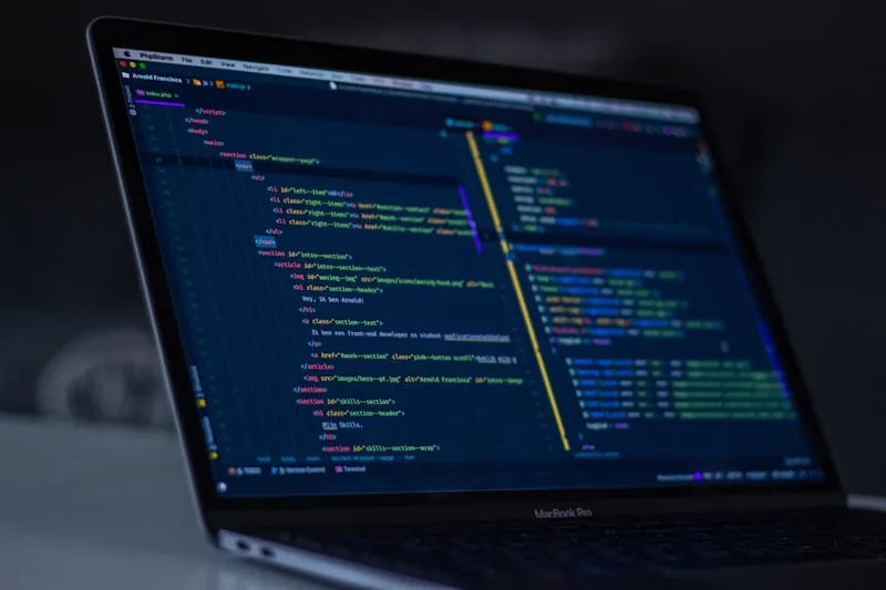 Notebook MacBook com código HTML no editor em tela, em ambiente escuro